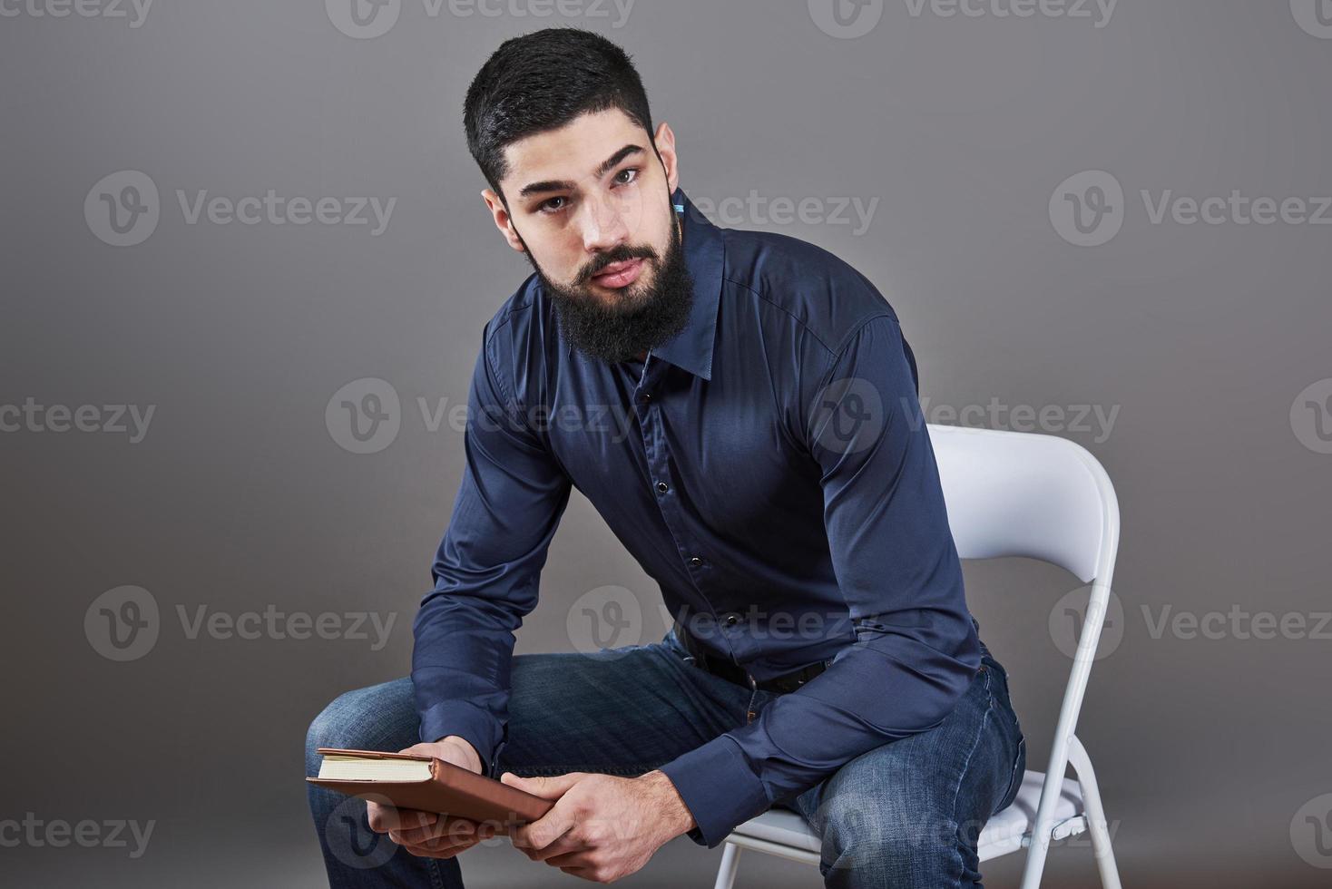 Portrait d'un bel homme barbu à pleines dents assis sur une chaise avec un livre sur les mains photo