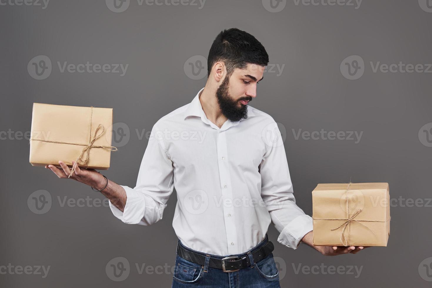 beau mec romantique regarde la boîte et fait un choix. tenant une grande boîte-cadeau pour son couple, sur fond gris. photo