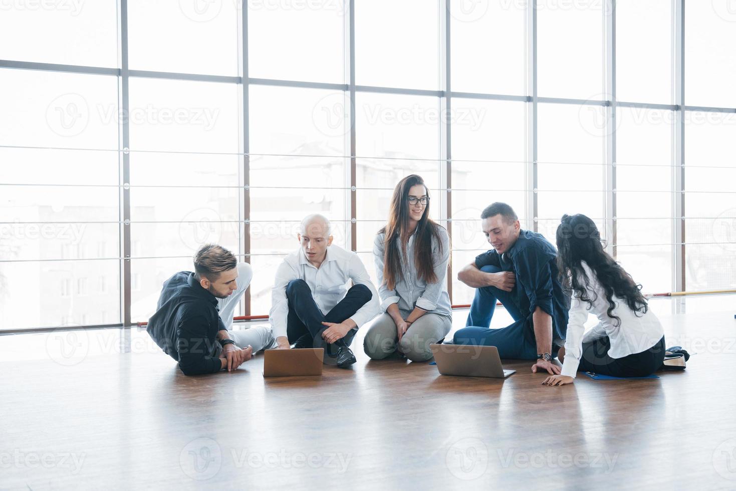 jeunes créatifs dans un bureau moderne. un groupe de jeunes gens d'affaires travaille avec un ordinateur portable. pigistes assis par terre. réalisation d'entreprise de coopération. concept de travail d'équipe photo