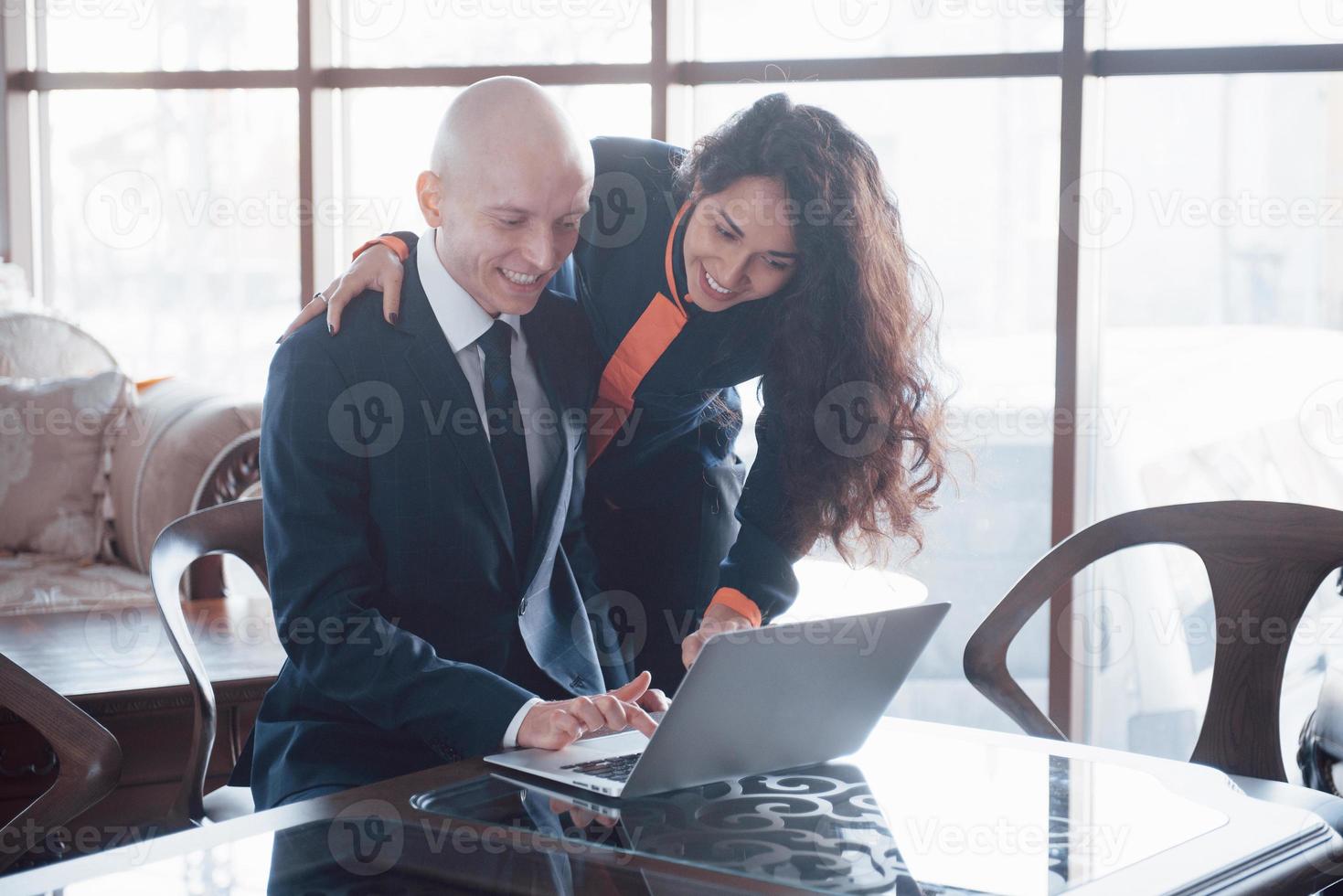 nous avons déjà d'excellents résultats. belle jeune femme pointant sur un ordinateur portable avec le sourire et discutant de quelque chose avec son collègue tout en se tenant au bureau photo