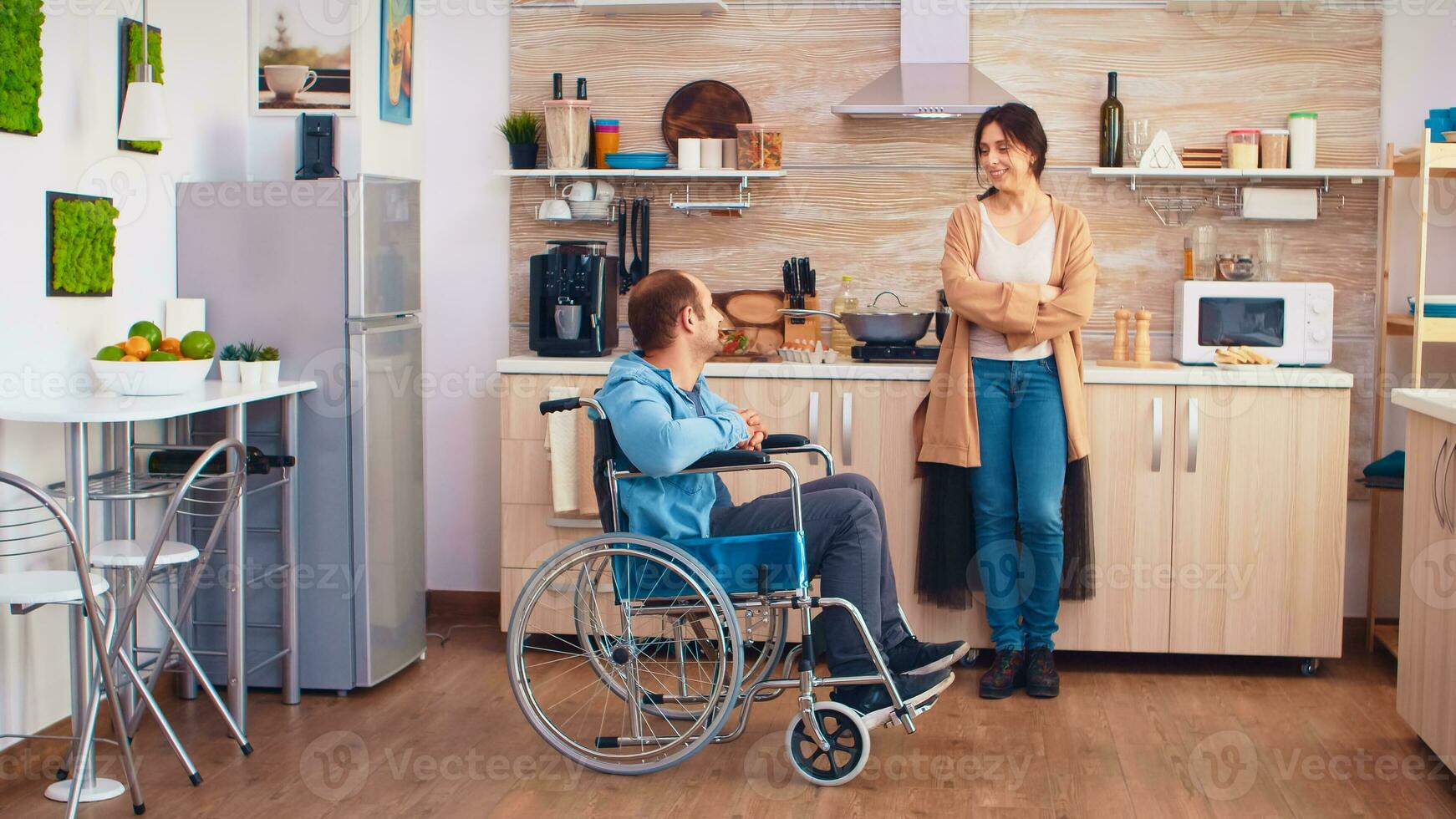 femme souriant à désactivée mari dans fauteuil roulant tandis que parlant avec lui. gars avec paralysie handicap invalidité handicapé des difficultés avoir Aidez-moi pour mobilité de l'amour et relation photo