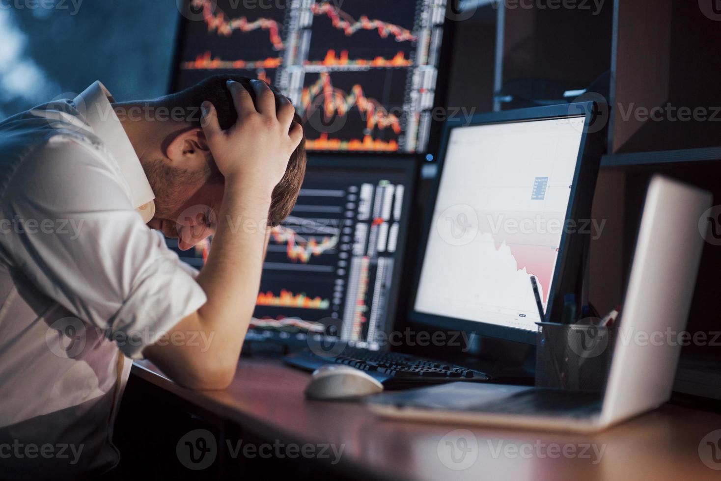 journée stressante au bureau. jeune homme d'affaires tenant la main sur son visage alors qu'il était assis au bureau dans un bureau de création. bourse trading forex finance concept graphique photo