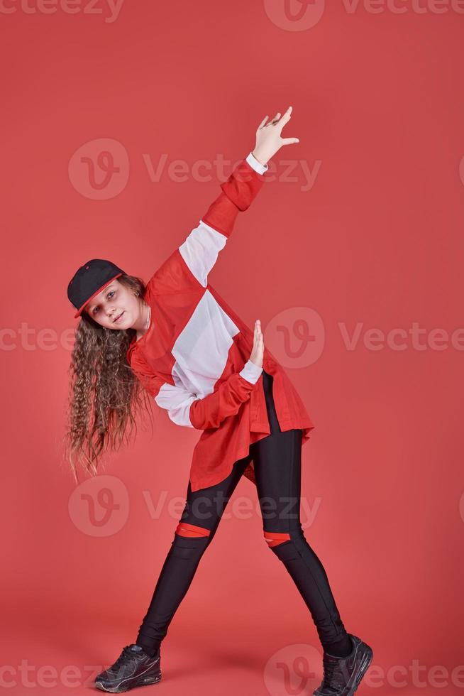 Jeune belle fille mignonne dansant sur fond rouge, adolescente moderne de style hip-hop mince sautant photo