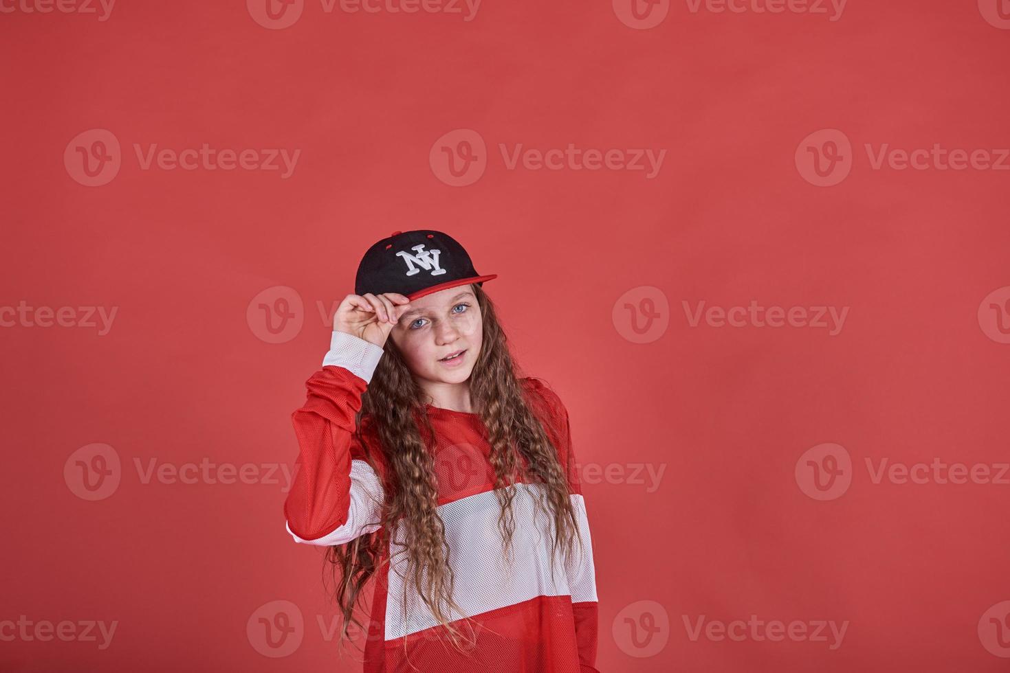 Jeune belle fille mignonne dansant sur fond rouge, adolescente moderne de style hip-hop mince sautant photo