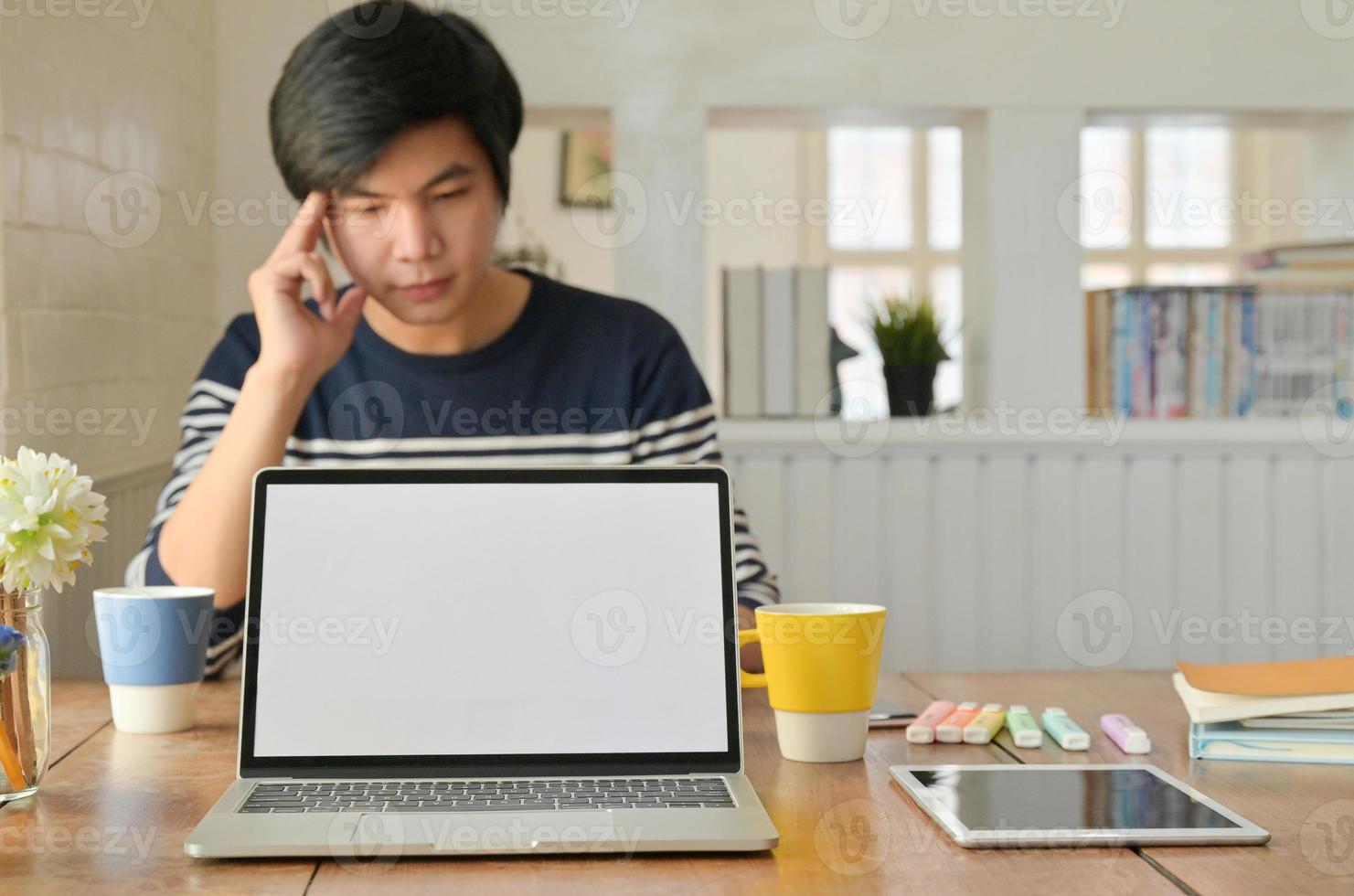 un ordinateur portable et un smartphone posés sur la table et un jeune homme est assis pour travailler à l'arrière. photo