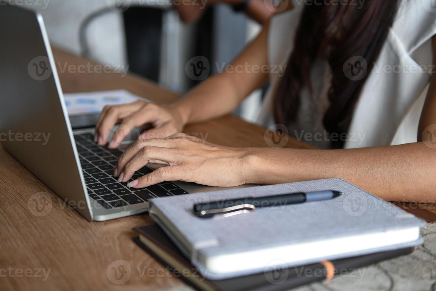 les cadres utilisent un ordinateur portable. elle a mis sa main sur le clavier. le devant a un cahier et un stylo posés sur la table. photo