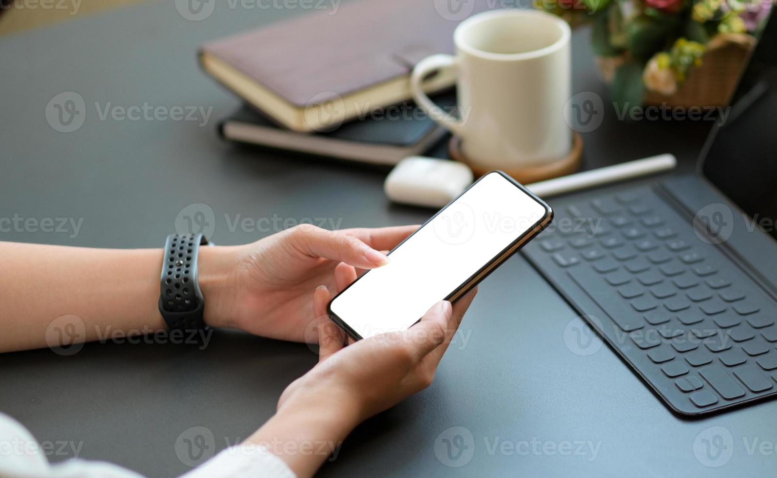 gros plan d'une jeune femme utilisant un smartphone à écran blanc avec un ordinateur portable et du café sur le bureau. photo