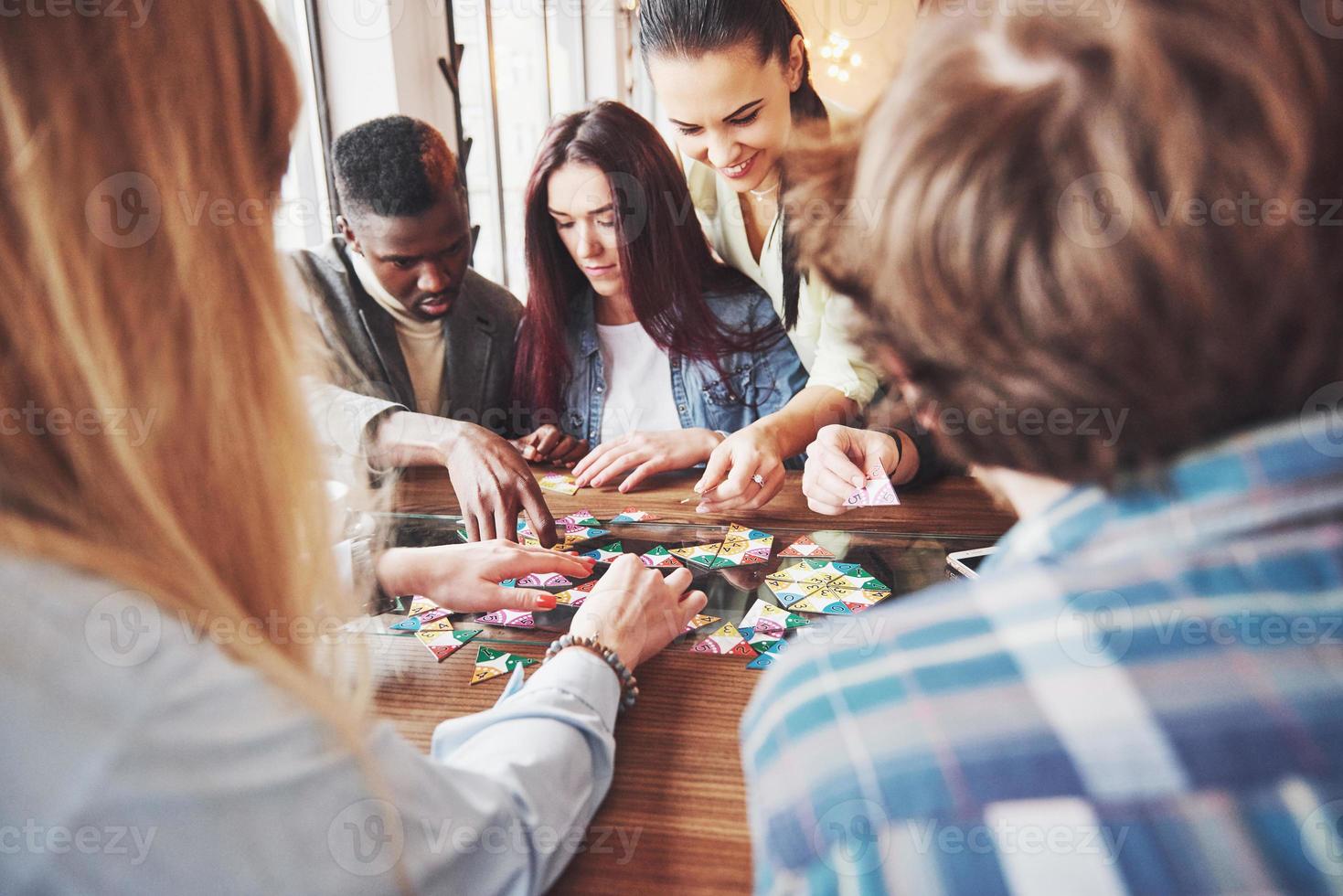 groupe d'amis multiethniques créatifs assis à une table en bois. les gens s'amusent en jouant à un jeu de société photo