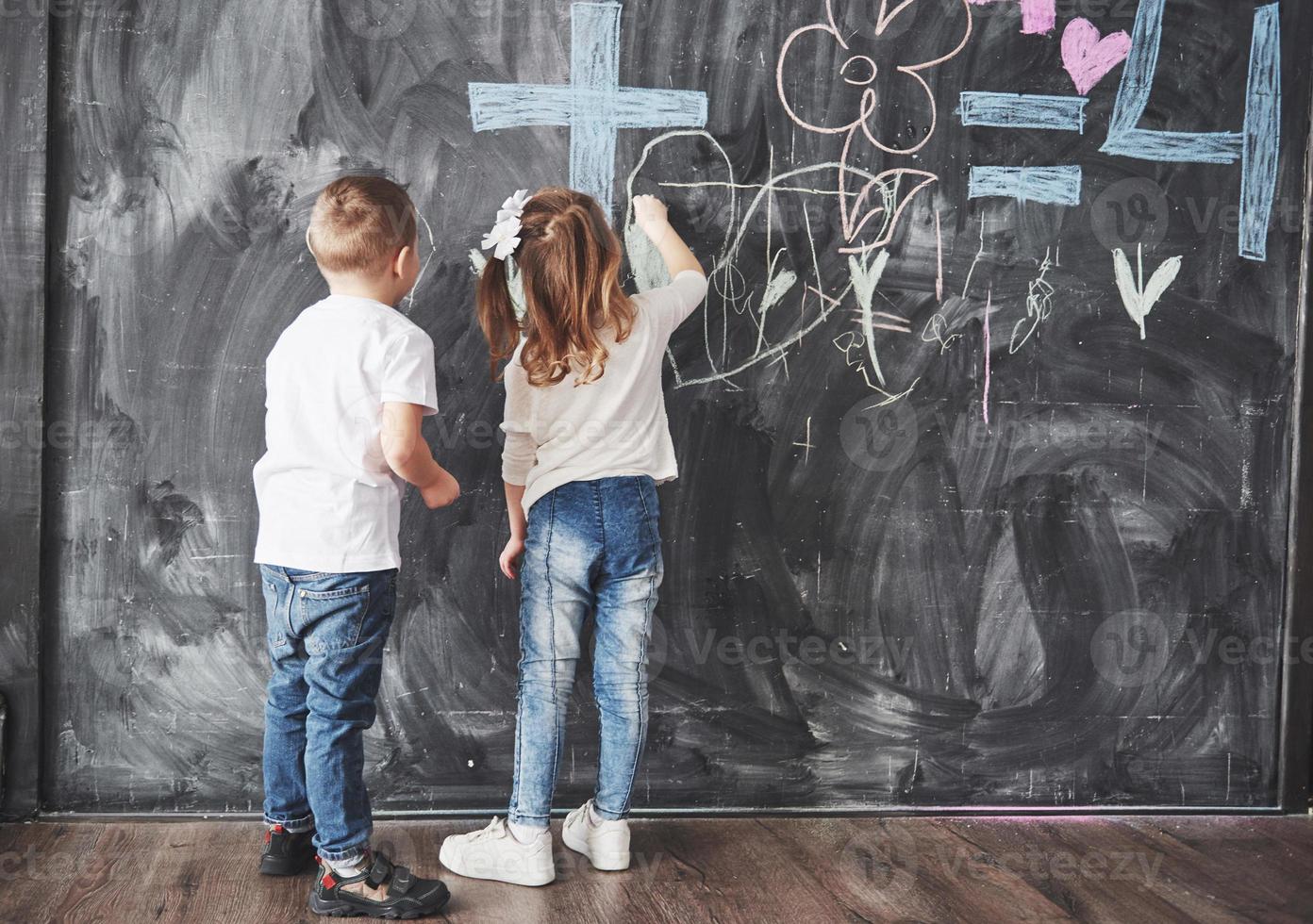 jolie petite fille et garçon dessinant avec la couleur du crayon sur le mur. œuvres d'enfant. Élève mignon écrivant sur le tableau photo