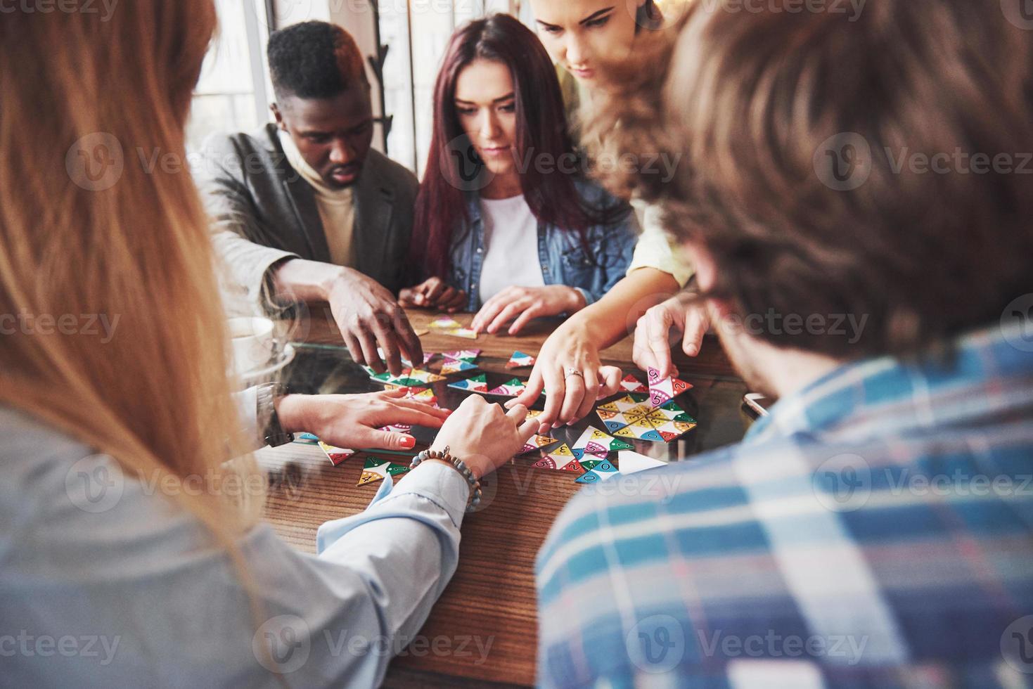 groupe d'amis créatifs assis à une table en bois. les gens s'amusent en jouant à un jeu de société photo