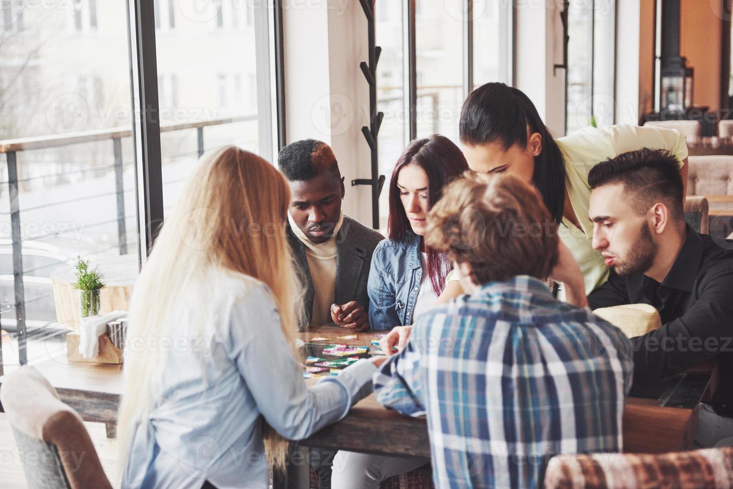 groupe d'amis créatifs assis à une table en bois. les gens s'amusent en jouant à un jeu de société photo