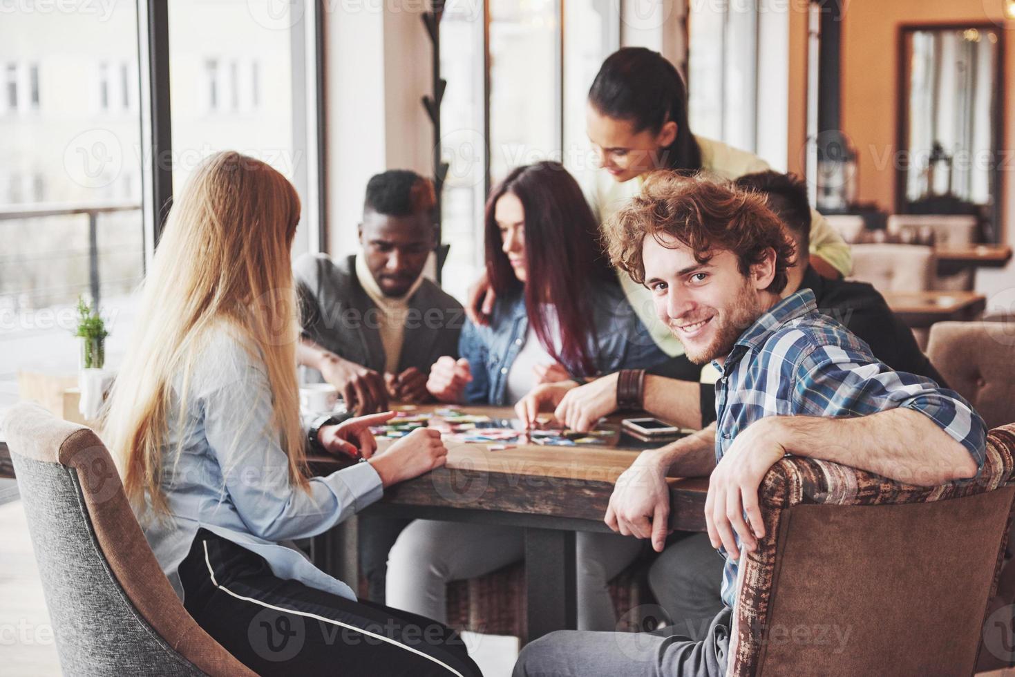 groupe d'amis créatifs assis à une table en bois. les gens s'amusent en jouant à un jeu de société photo