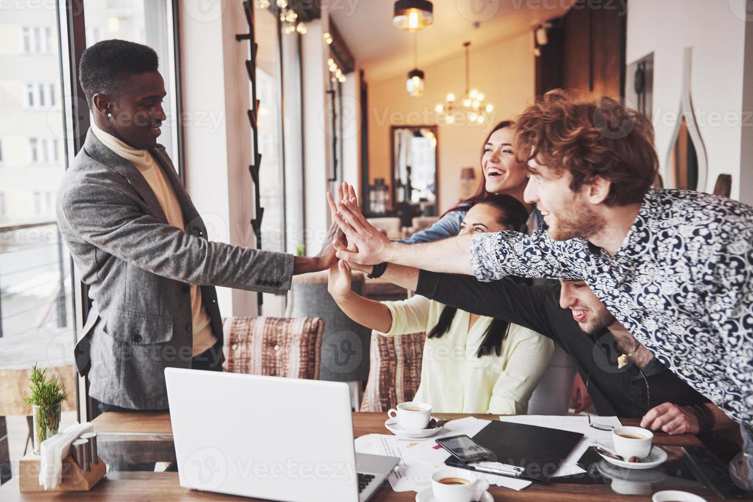 jeunes entrepreneurs heureux dans des vêtements décontractés à la table d'un café ou dans un bureau d'affaires se donnant des coups de chapeau comme s'ils célébraient le succès ou lançaient un nouveau projet photo