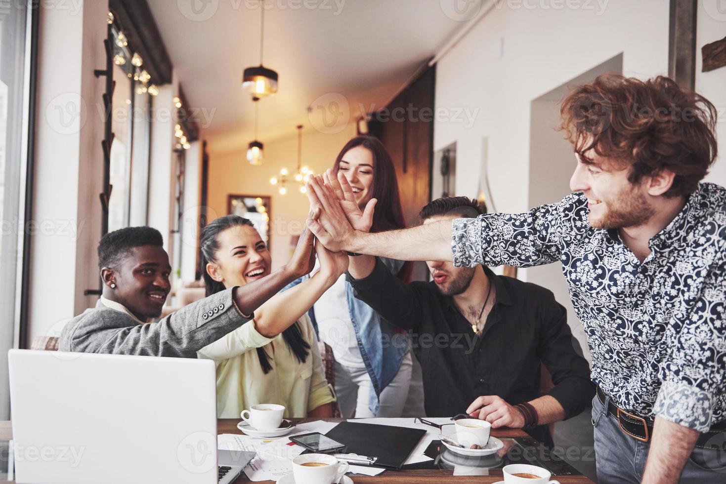 jeunes entrepreneurs heureux dans des vêtements décontractés à la table d'un café ou dans un bureau d'affaires se donnant des coups de chapeau comme s'ils célébraient le succès ou lançaient un nouveau projet photo