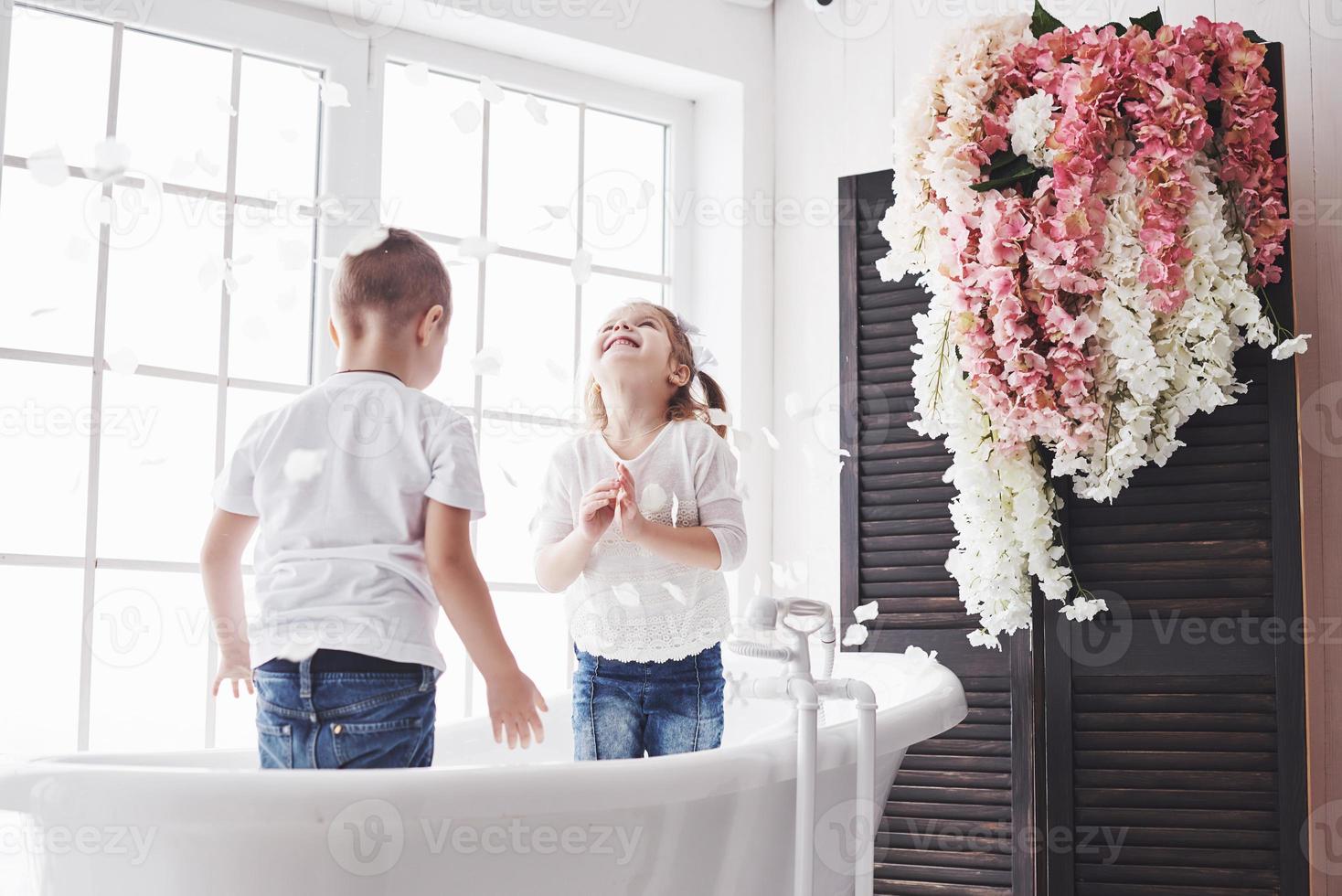 enfant jouant avec des pétales de rose dans la salle de bain à domicile. petite fille et garçon s'amusant et s'amusant ensemble. le concept de l'enfance et la réalisation des rêves, de la fantaisie, de l'imagination photo