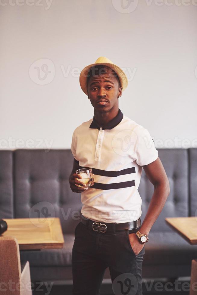 homme afro-américain à la mode au chapeau avec verre de whisky photo