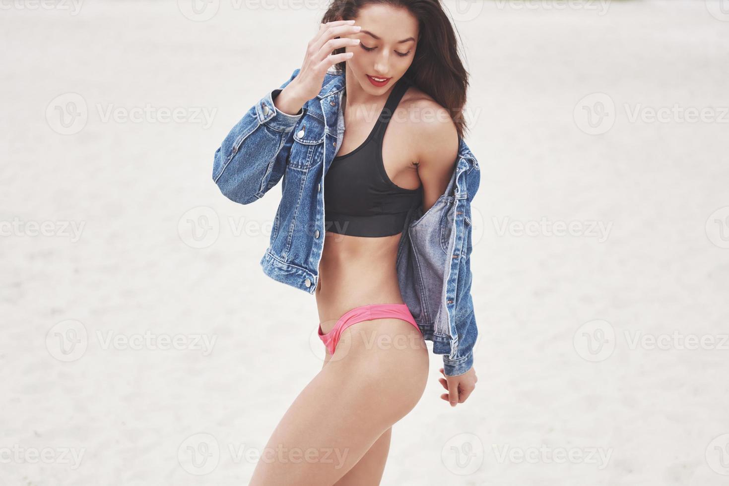 belle fille de luxe mince en bikini et jeans jaket sur la plage de sable sur une île tropicale. corps bronzé sexy et silhouette parfaite photo