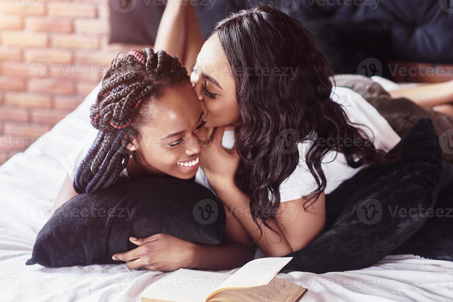 deux belles filles africaines en vêtements de nuit souriantes assises sur le lit à la maison se sont réveillées le matin par une journée ensoleillée. photo