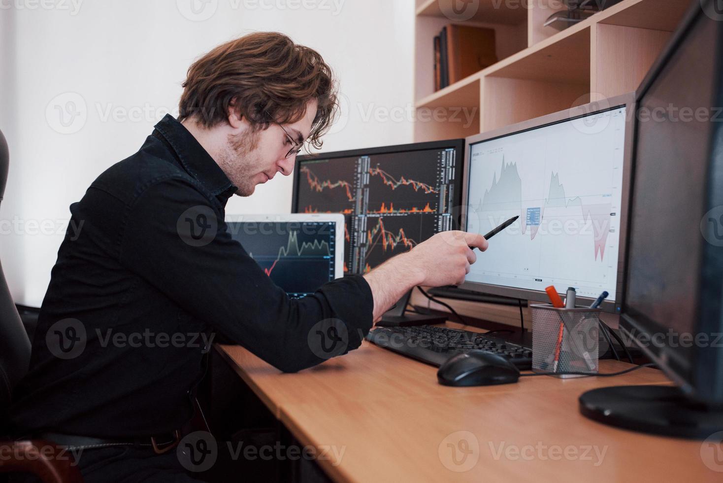 journée stressante au bureau. jeune homme d'affaires tenant la main sur son visage alors qu'il était assis au bureau dans un bureau de création. bourse trading forex finance concept graphique photo