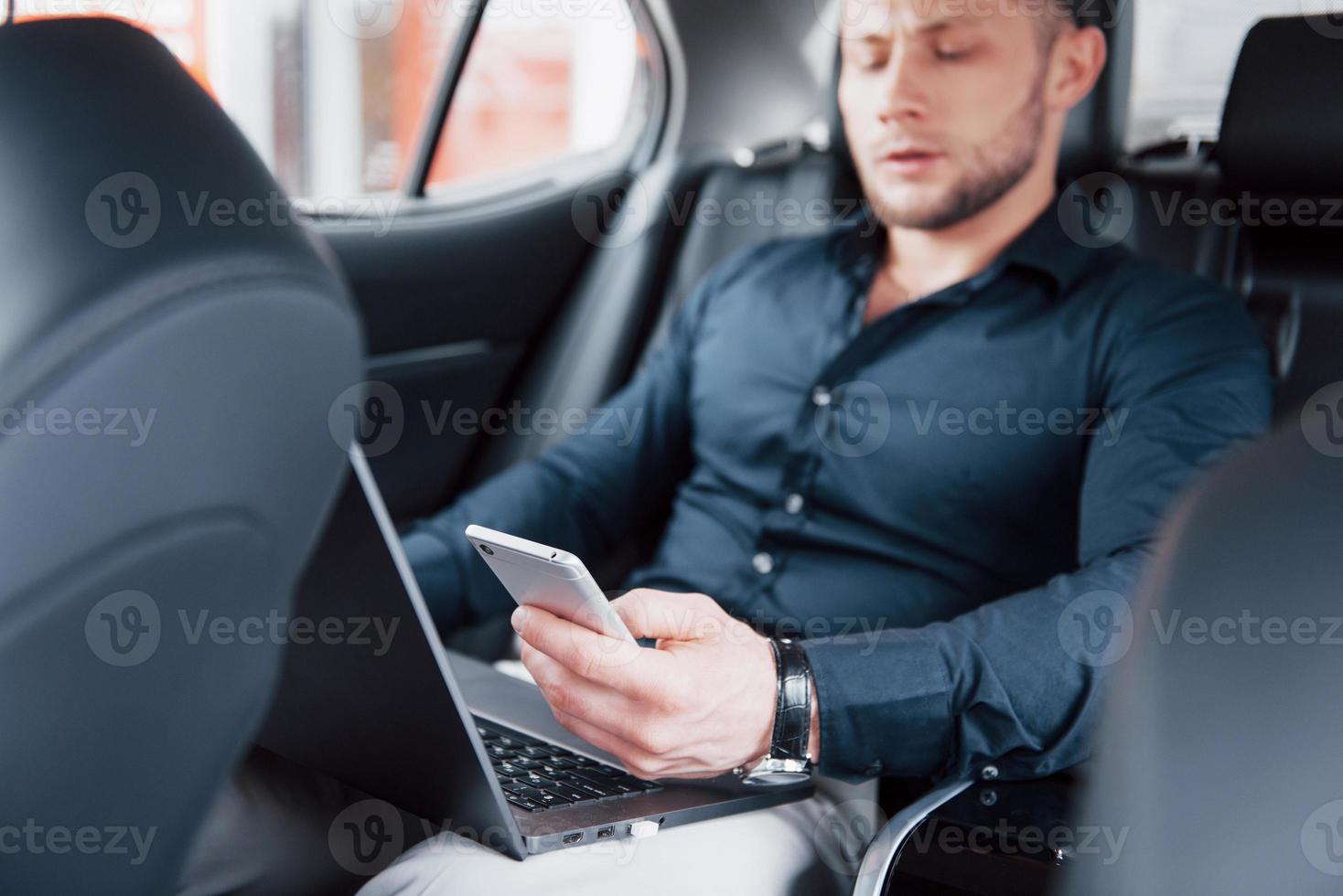 un jeune homme d'affaires travaillant sur un ordinateur portable et parlant au téléphone alors qu'il était assis à l'arrière de la voiture. travaille en mouvement, apprécie son temps photo