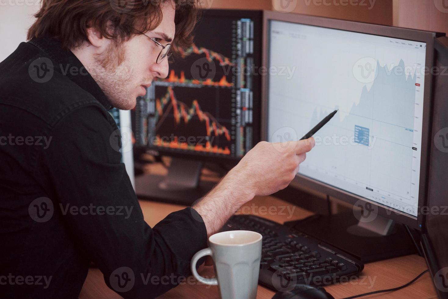 journée stressante au bureau. jeune homme d'affaires tenant la main sur son visage alors qu'il était assis au bureau dans un bureau de création. bourse trading forex finance concept graphique photo