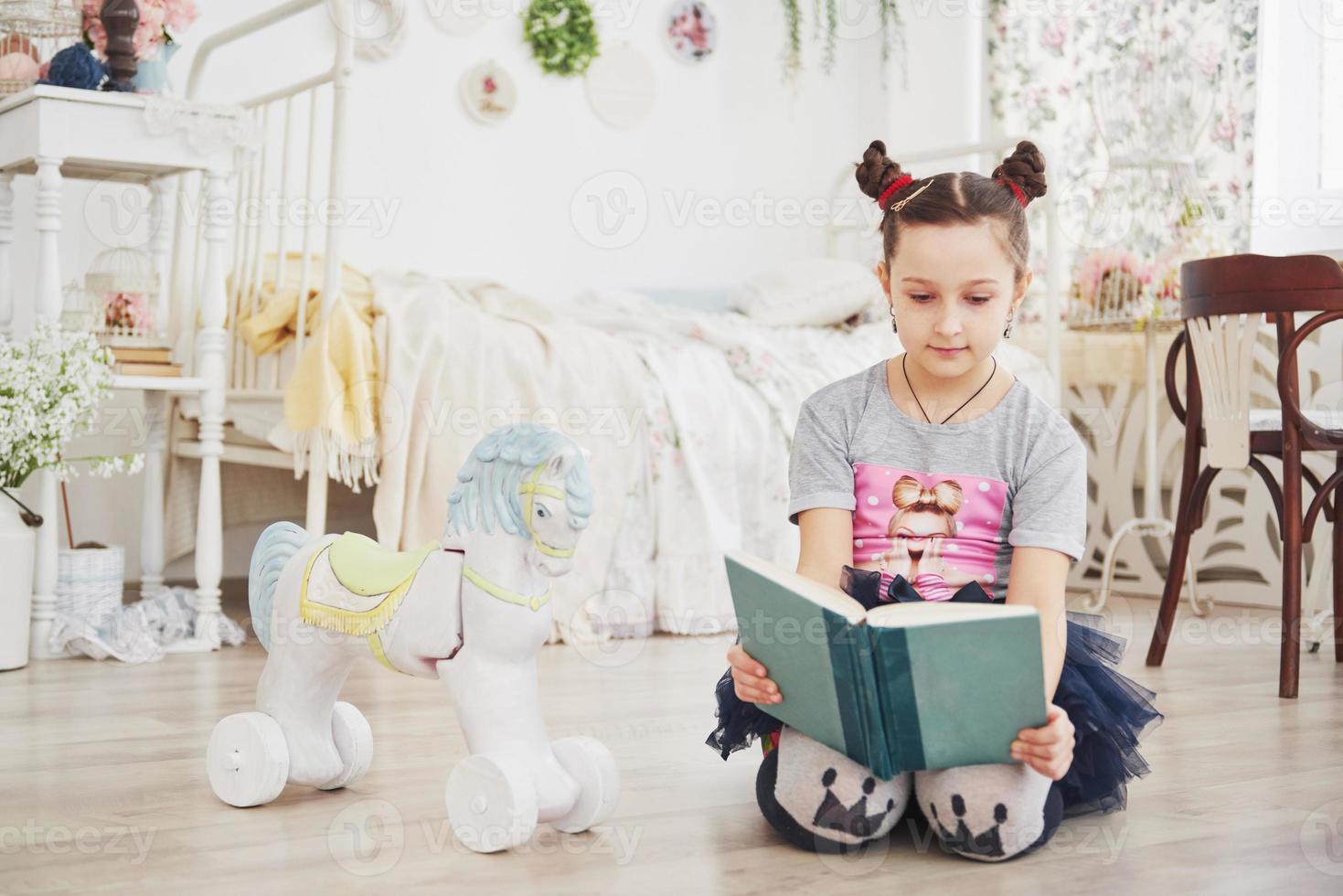 mignonne petite fille enfant lisant un livre dans la chambre. enfant avec couronne assis sur le lit près de la fenêtre photo