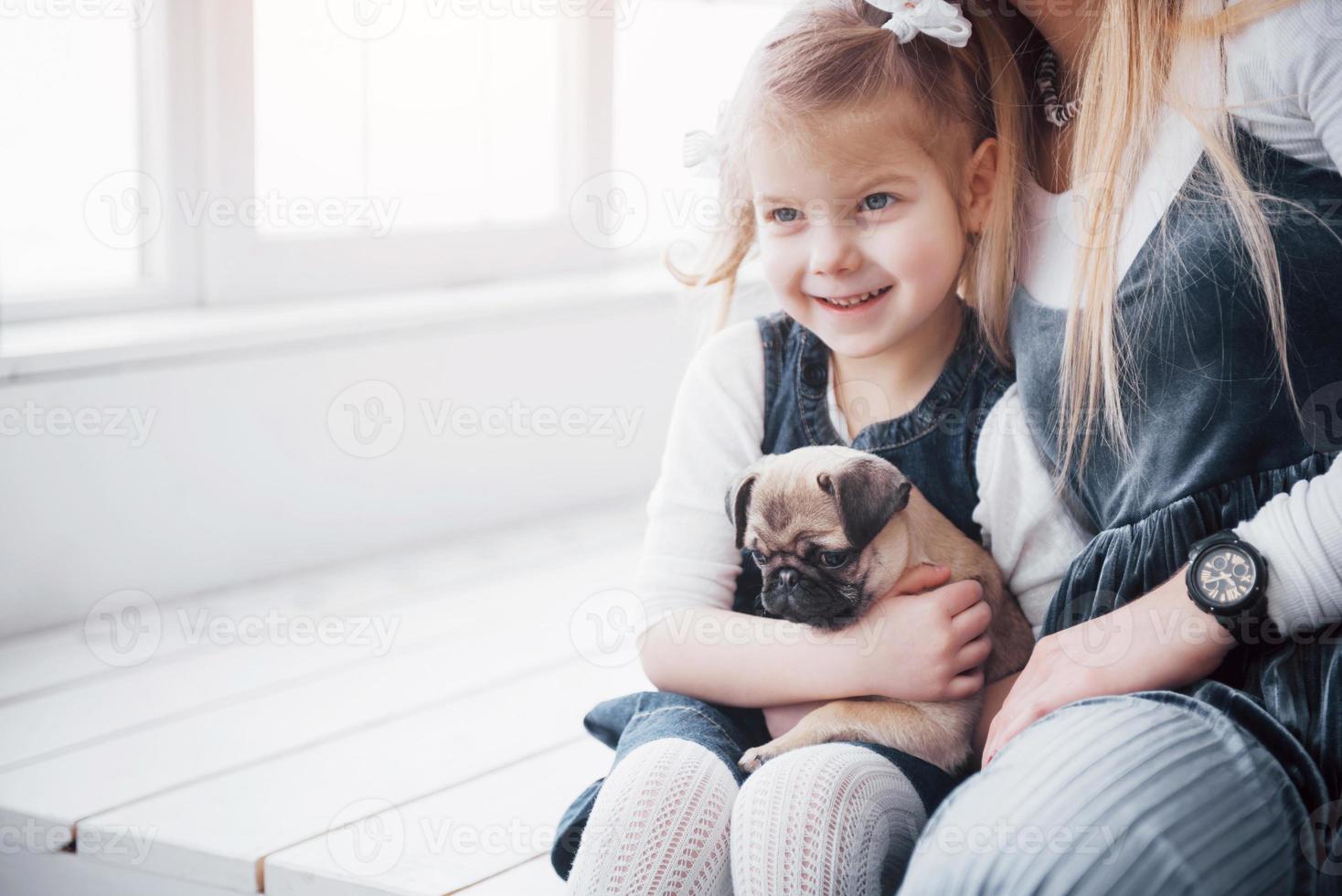 famille aimante heureuse. mère et sa fille enfant fille jouant et étreignant adorable carlin photo