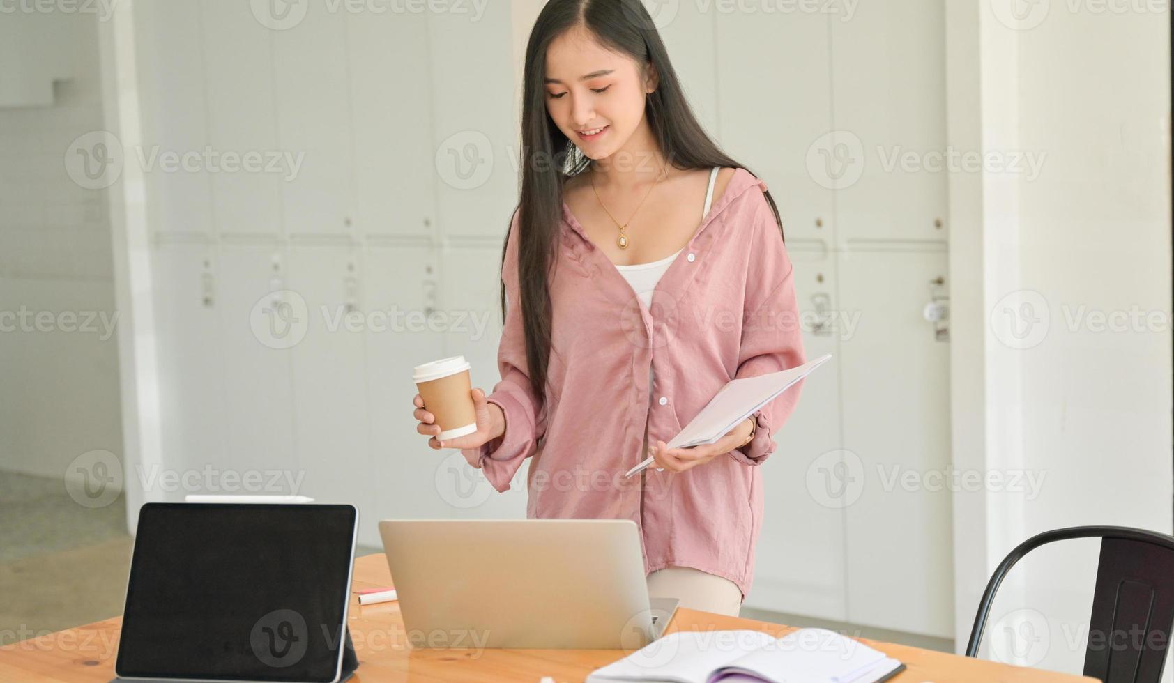 une étudiante tenant une tasse de café et un document à la main avec un ordinateur portable sur la table. photo