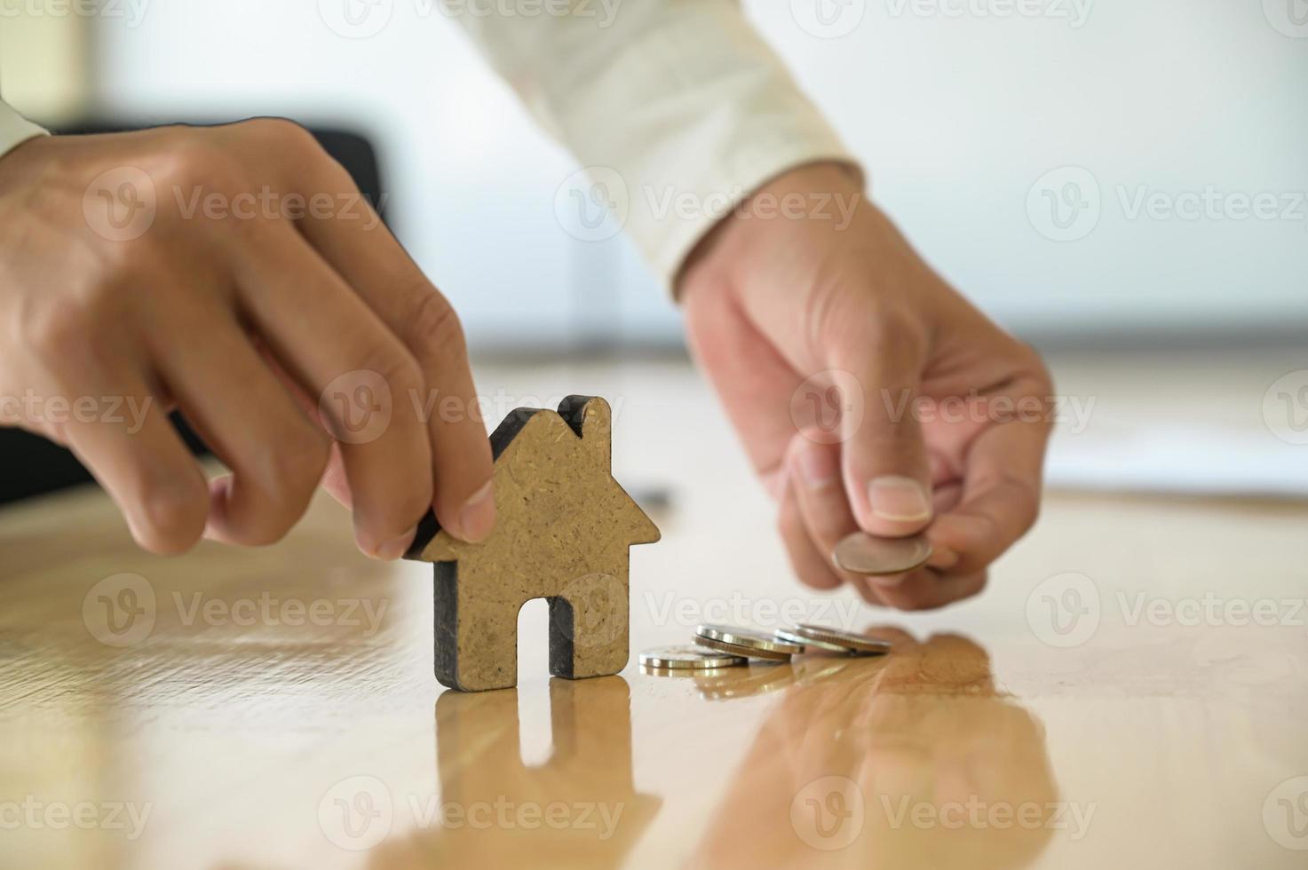 concept de commerce de maison, la main de personnes tenant un modèle de maison en bois et pièces de monnaie. photo