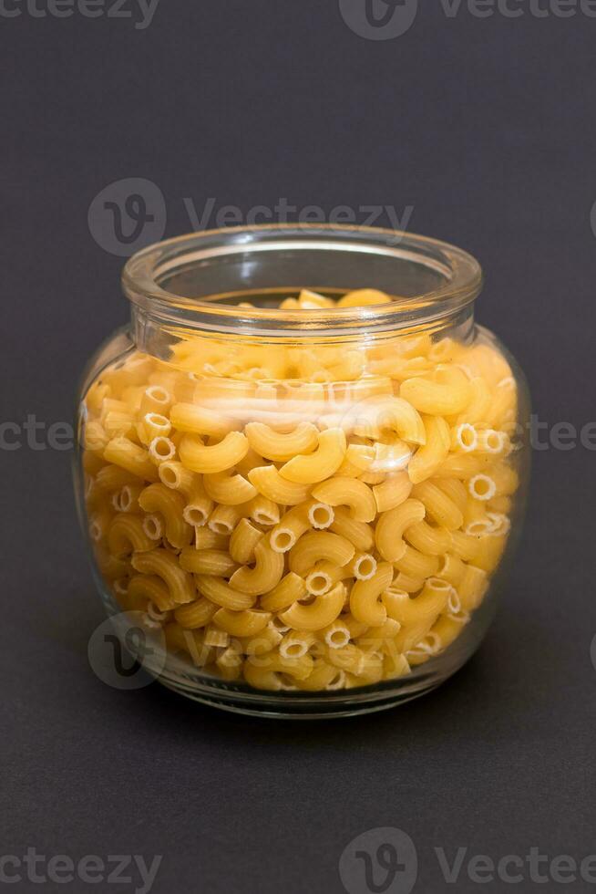 non cuit chifferi rigati Pâtes dans verre pot sur noir Contexte. graisse et mauvais pour la santé aliments. classique sec macaroni. italien culture et cuisine. brut Pâtes photo