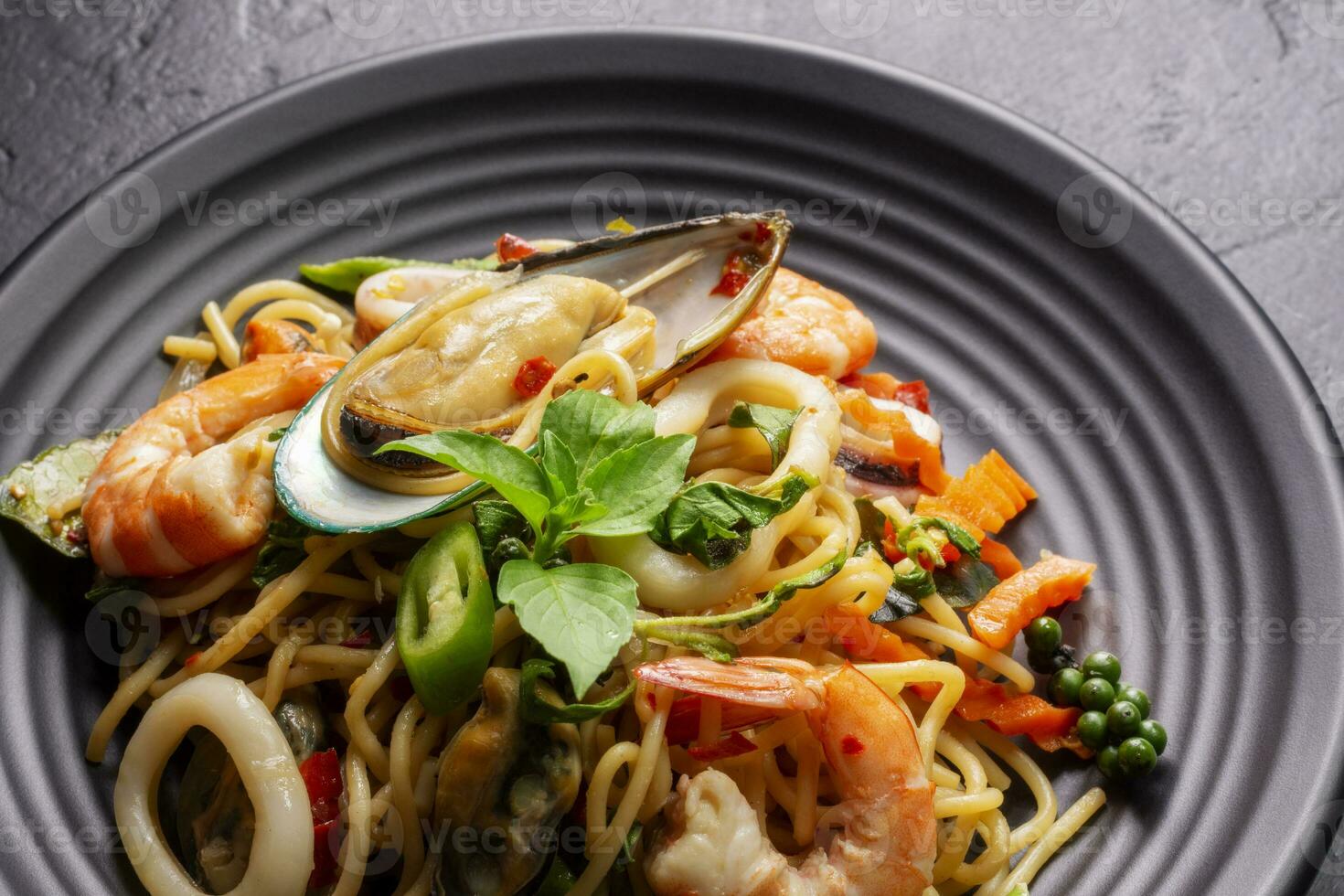 fermer de ivre spaghetti avec Fruit de mer avec crevette, calmar, palourdes, le Chili, et basilic. en bonne santé thaïlandais asiatique nourriture dans une assiette sur une noir Contexte tableau. photo