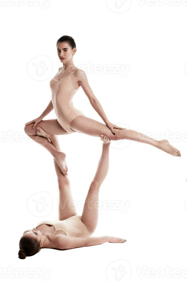 deux souple les filles gymnastes dans beige justaucorps sont performant des exercices à l'envers vers le bas en utilisant soutien et posant isolé sur blanc Contexte. fermer. photo