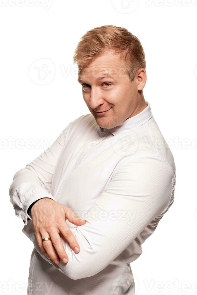 imposant, jeune, blond homme dans une blanc chemise est grimaçant tandis que permanent isolé sur une blanc Contexte photo