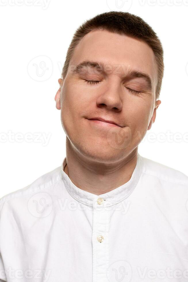 charmant Beau Jeune homme dans une blanc chemise est fabrication visages, tandis que permanent isolé sur une blanc Contexte photo