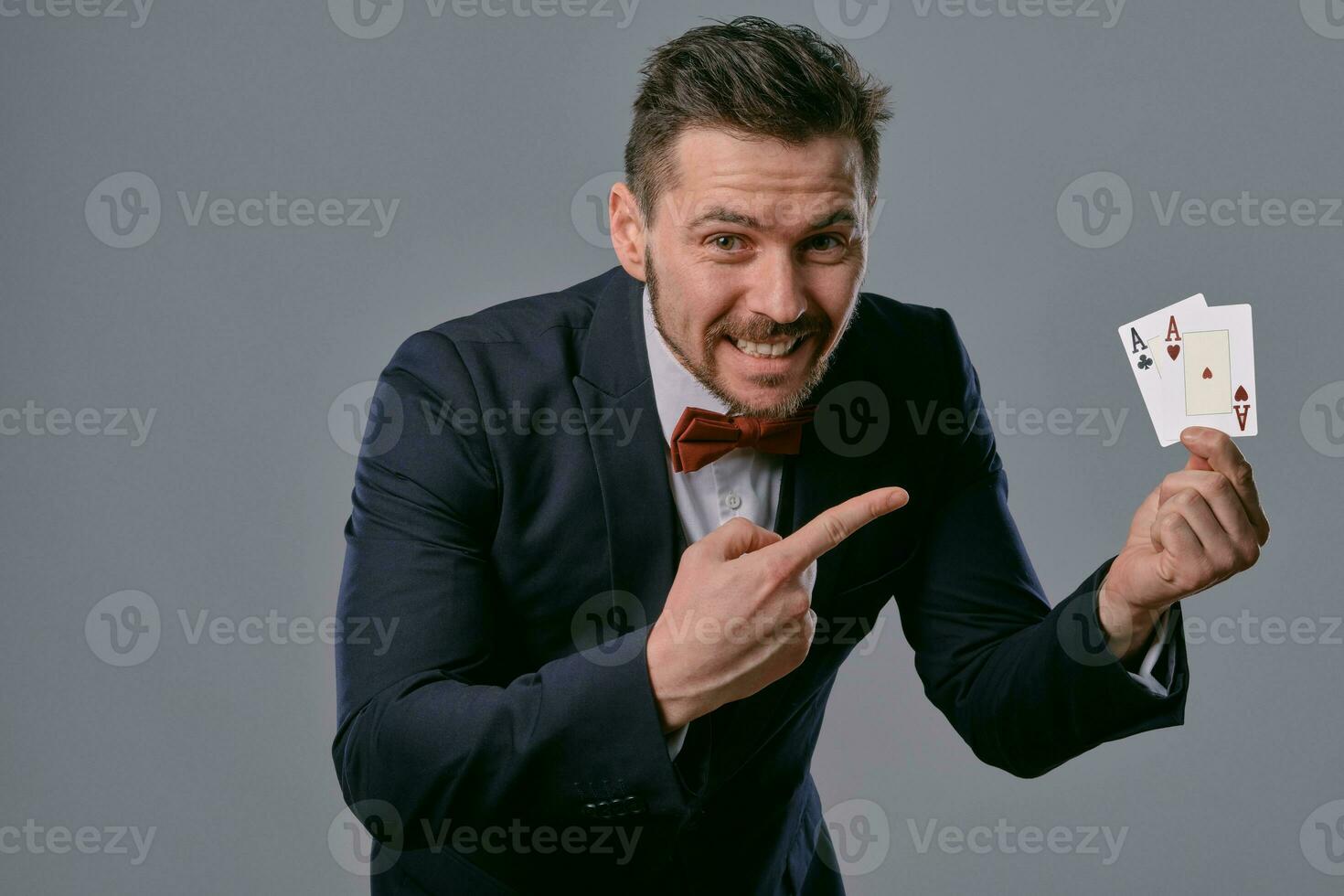 homme dans noir classique costume et rouge nœud papillon montrant deux en jouant cartes tandis que posant contre gris studio Contexte. jeu, poker, casino. fermer. photo