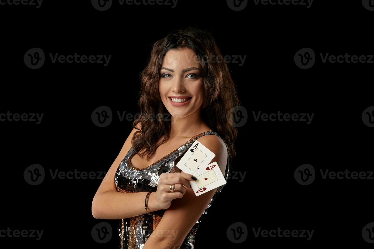 brunette fille dans une coloré paillette robe posant en portant deux en jouant cartes, permanent contre noir studio Contexte. casino, poker. fermer. photo