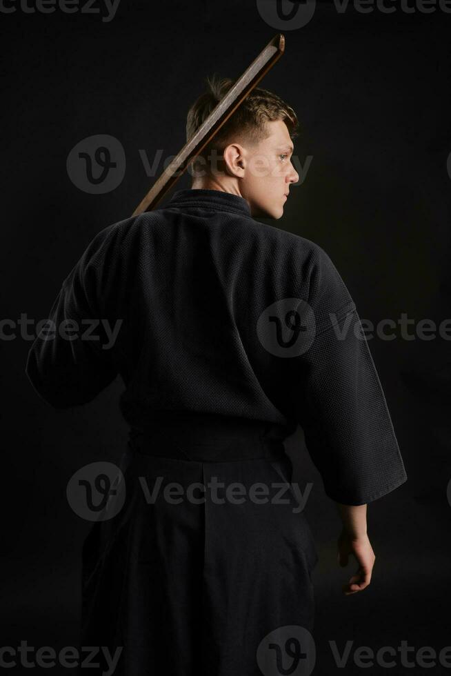 kendo gourou portant dans une traditionnel Japonais kimono est pratiquant martial art avec le shinaï bambou épée contre une noir studio Contexte. photo