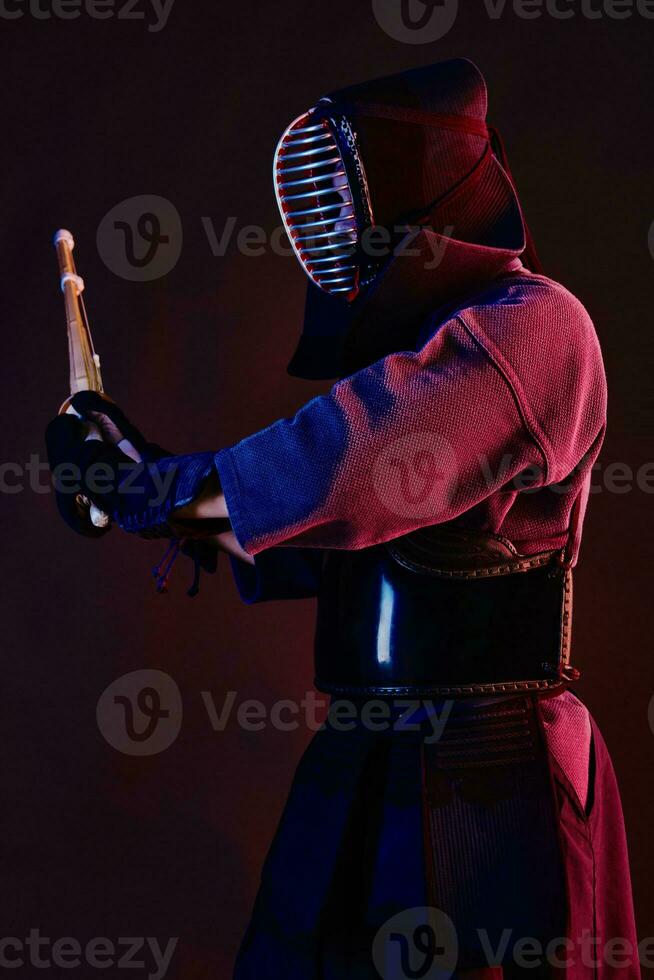 proche en haut tir, kendo combattant portant dans un armure, traditionnel kimono, casque pratiquant martial art avec shinaï bambou épée, noir Contexte. photo