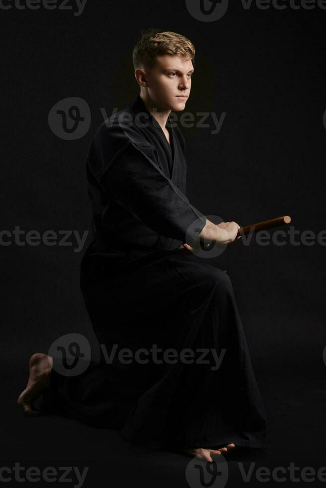 kendo gourou portant dans une traditionnel Japonais kimono est pratiquant martial art avec le shinaï bambou épée contre une noir studio Contexte. photo