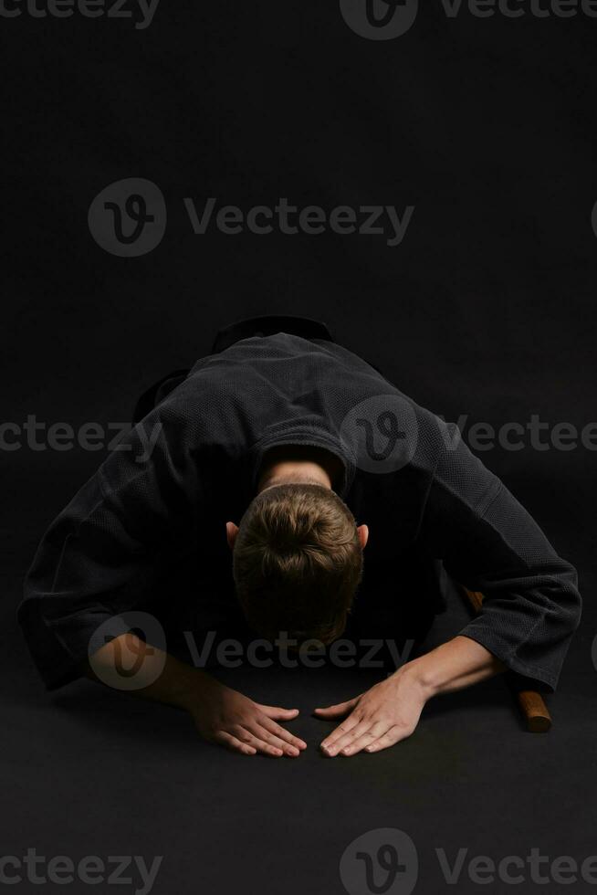 kendo gourou portant dans une traditionnel Japonais kimono est pratiquant martial art avec le shinaï bambou épée contre une noir studio Contexte. photo