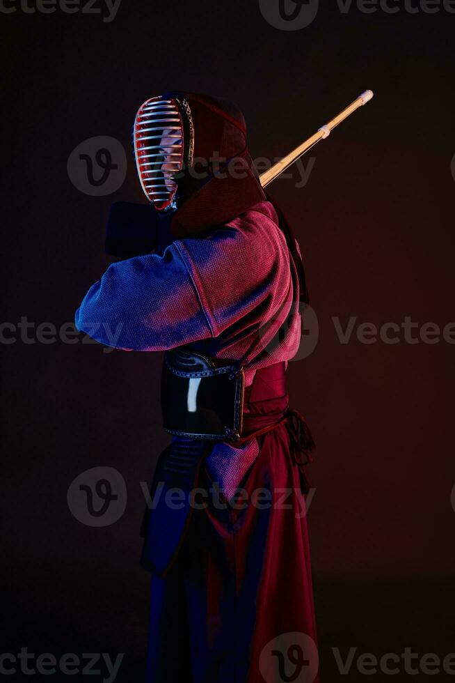 proche en haut tir, kendo combattant portant dans un armure, traditionnel kimono, casque pratiquant martial art avec shinaï bambou épée, noir Contexte. photo