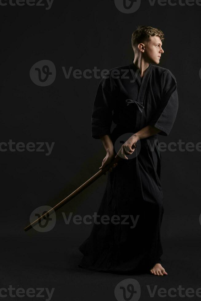 kendo gourou portant dans une traditionnel Japonais kimono est pratiquant martial art avec le shinaï bambou épée contre une noir studio Contexte. photo