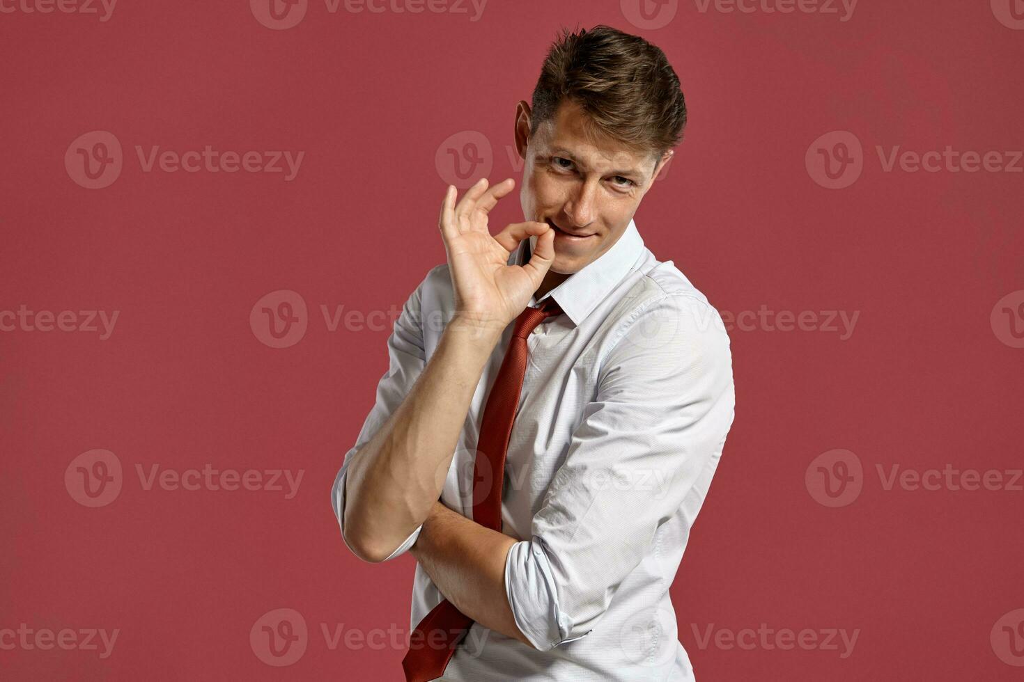 Jeune homme dans une classique blanc chemise et rouge attacher posant plus de une rose Contexte. photo