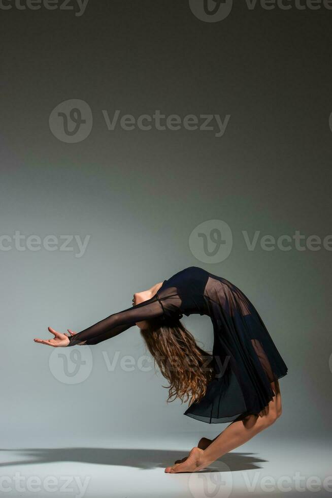 Jeune magnifique Danseur dans noir robe posant sur une foncé gris studio Contexte photo