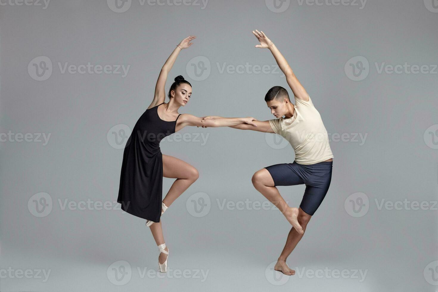deux athlétique moderne ballet danseurs sont posant contre une gris studio Contexte. photo