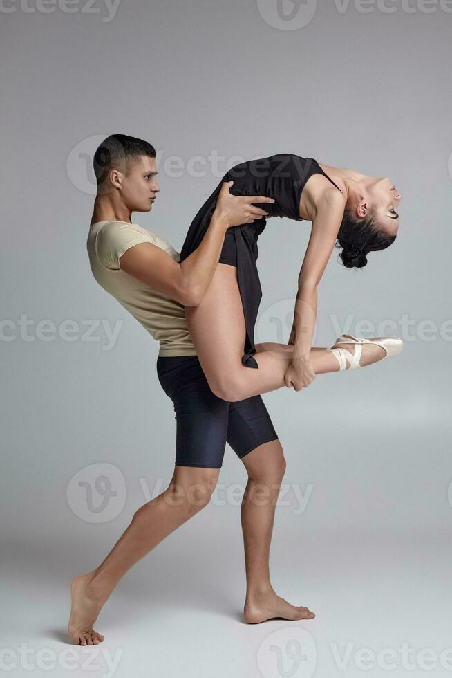 deux athlétique moderne ballet danseurs sont posant contre une gris studio Contexte. photo