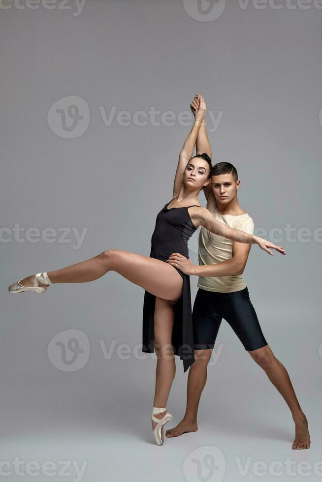 deux athlétique moderne ballet danseurs sont posant contre une gris studio Contexte. photo