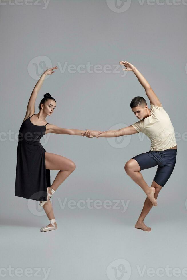 deux athlétique moderne ballet danseurs sont posant contre une gris studio Contexte. photo