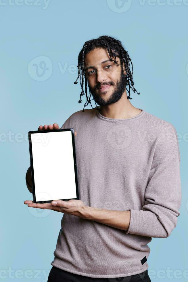 Beau arabe homme en présentant numérique tablette avec Vide toucher écran pour publicité moquer en haut. souriant la personne montrant dispositif avec blanc afficher et copie espace pour Logiciel app commercialisation promotion photo