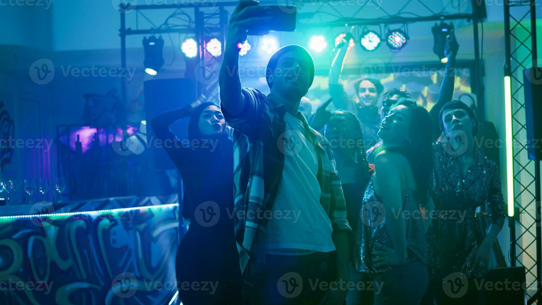 copains prise des photos à boîte de nuit, faire la fête ensemble en dessous de déconcerte. groupe de Hommes et femmes ayant amusement à fête un événement avec électronique musique, prise Photos et tournage. ordinateur de poche tir.